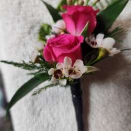 Pink rose boutonniere with white accent flowers and dark ribbon