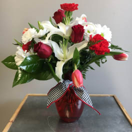 Red and white flower arrangement in a red vase with a checkered ribbon