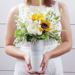 Woman holding a white and yellow flower arrangement in a gray vase