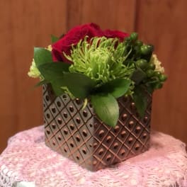 Compact floral arrangement in a patterned metal container with red and green blooms