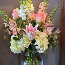 Tall arrangement of pink lilies and roses with white hydrangeas in a clear glass vase