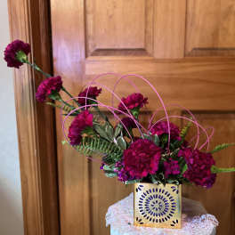 Magenta carnations in a gold square vase with pink wire loops