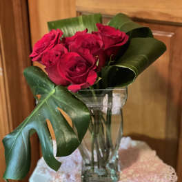 Red roses in a clear glass vase with large tropical leaves