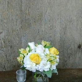 Yellow and white roses in a square glass vase with white hydrangeas