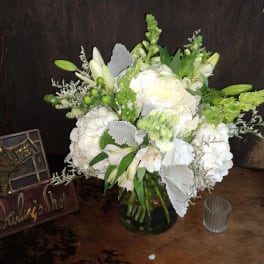 White floral arrangement in a glass vase with green accents