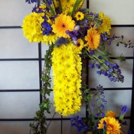 Cross-shaped floral arrangement with yellow and orange daisies and blue flowers