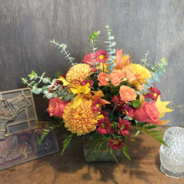 Mixed bouquet in a square glass vase with pink, orange, and yellow flowers