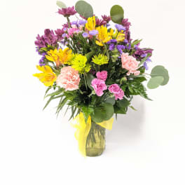 Mixed bouquet of yellow, pink, and purple flowers in a glass vase