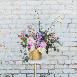 Pastel floral arrangement in a gold vase on a small round table