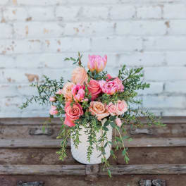 Pink and peach roses in a white vase with trailing greenery