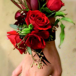 Wrist corsage with red roses and dark purple calla lilies on a black band