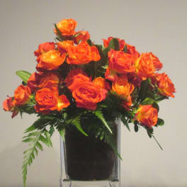 Orange and yellow spray roses arranged in a clear glass cube vase