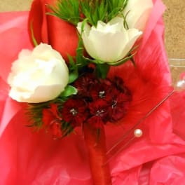Red and white rose boutonniere with small red blooms, wrapped in red ribbon on pink tissue paper