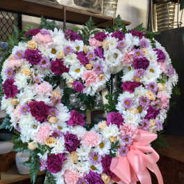 Heart-shaped floral wreath with pink ribbon and mixed pink, white, and purple flowers
