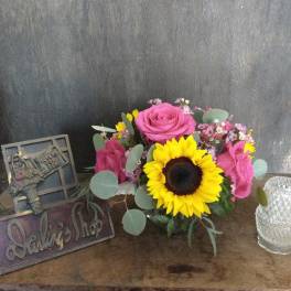 Pink roses and a sunflower in a low glass vase with small filler flowers