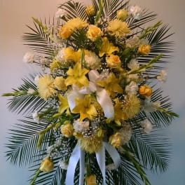 Standing floral spray with yellow lilies and roses on a white ribboned easel
