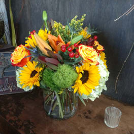 Mixed bouquet in a clear glass vase with sunflowers, roses, and lilies