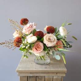 Pink and white roses in a clear glass vase with orange pom-pom flowers