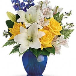 Bouquet of white lilies, yellow roses, and blue flowers in a blue vase