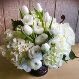 White floral arrangement with tulips, roses, ranunculus, and hydrangeas in a dark vase