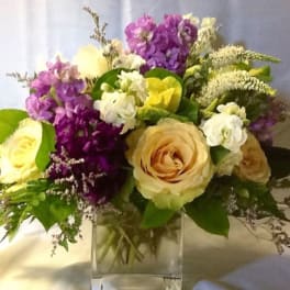 Bouquet of cream roses and purple flowers in a clear glass vase