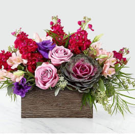 Pink and red floral arrangement in a wooden box with purple accents