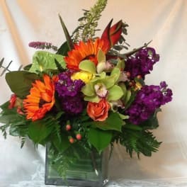 Bright mixed bouquet in a square glass vase with orange, purple, and green flowers