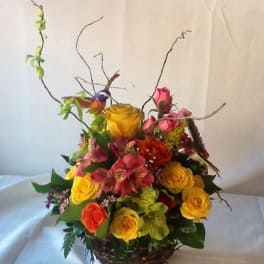 Colorful rose arrangement in a wicker basket with tall curly branches
