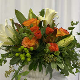 Orange and white roses arranged in a white vase with greenery