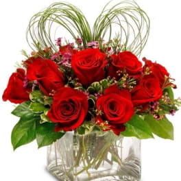 Red roses arranged in a clear square vase with decorative loops