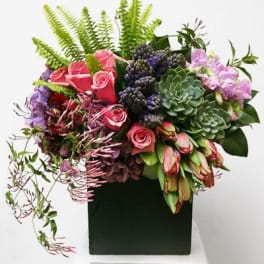 Mixed bouquet with pink roses, succulents, and purple blooms in a black container