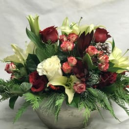 Holiday floral arrangement with roses, lilies, and greenery in a round vase