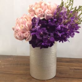 Pink roses and purple orchids arranged in a white vase