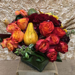 Bouquet of red and orange roses with decorative gourds in a vase