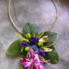 Floral necklace with purple orchid blooms and green leaves on a gold hoop