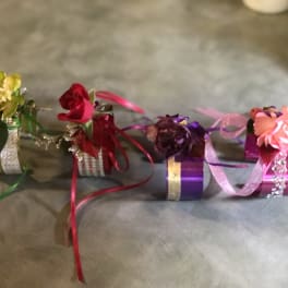 Four small floral wrist corsages with ribbon accents on a gray surface
