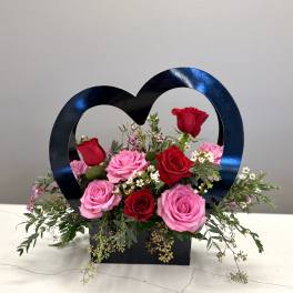 Heart-shaped floral arrangement with pink and red roses in a black box