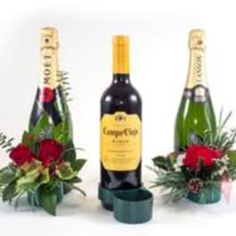 Two champagne bottles with red rose arrangements and greenery