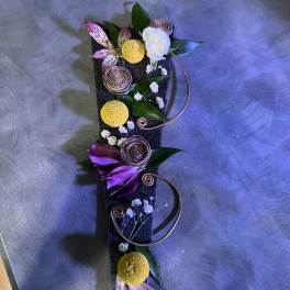 Vertical floral arrangement on a dark rectangular base with purple and yellow blooms
