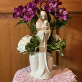 Purple and white flowers arranged around a ceramic Madonna and child figurine