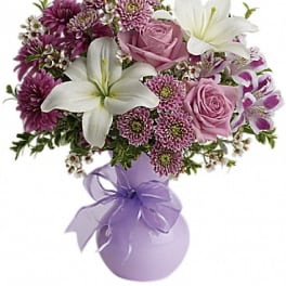 Pink roses and white lilies in a lavender vase with a ribbon