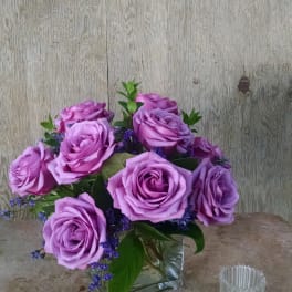 Lavender rose bouquet in a clear square vase with purple filler flowers
