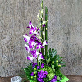 Purple orchids in a green square vase with a small glass candle holder