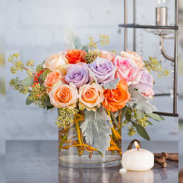 Mixed roses in a clear glass vase beside a lit candle