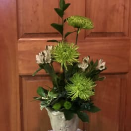 Tall green and white floral arrangement in a decorative urn