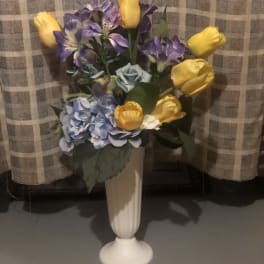 Bouquet of yellow tulips, purple alstroemeria, and blue hydrangeas in a white vase