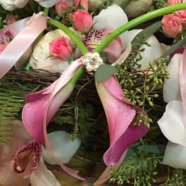 Pink calla lilies, spray roses, and orchids with pink ribbon and pearls in a lush mixed arrangement