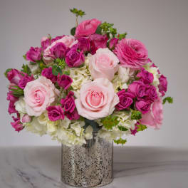 Round arrangement of light and hot pink roses with white hydrangeas in a silver cylinder vase
