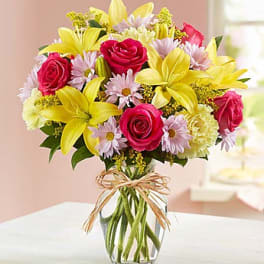 Bouquet of pink roses, yellow lilies, and pale daisies in a glass vase