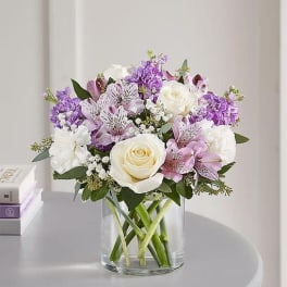 Bouquet of white roses and purple flowers in a clear glass vase